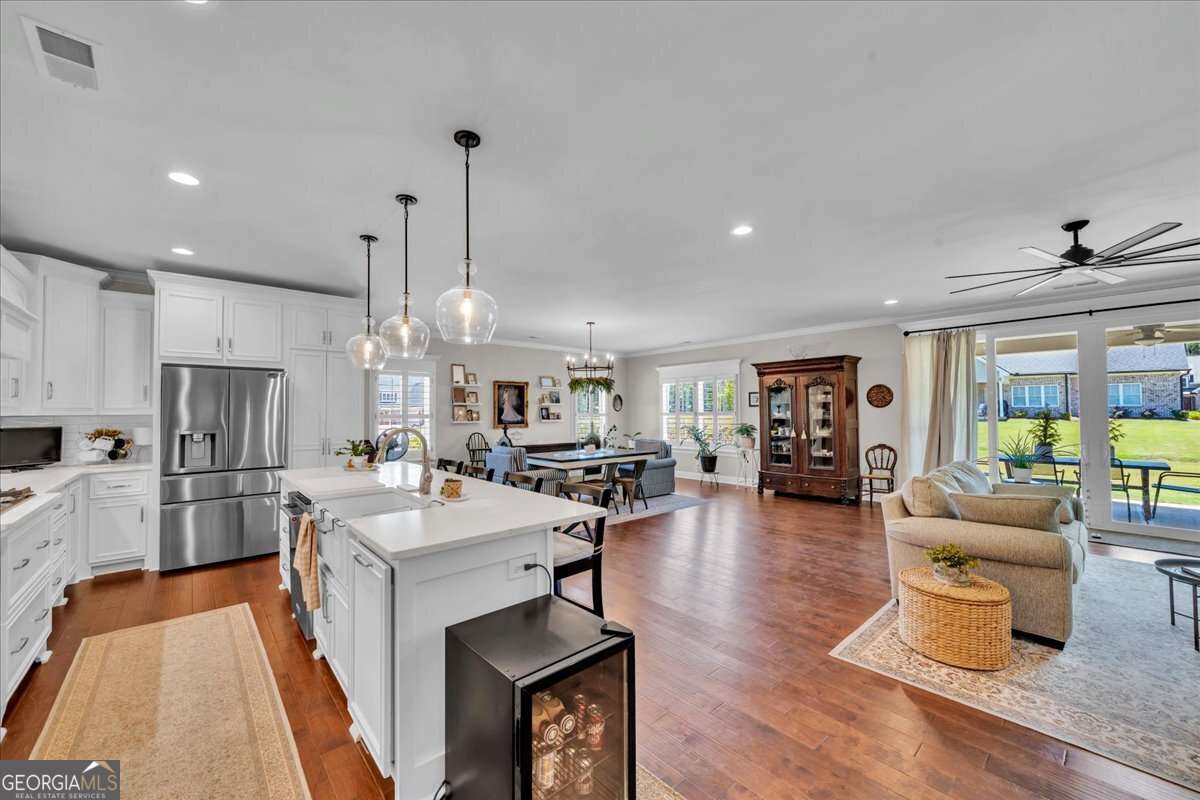 Open-concept kitchen and living area featuring a large island with seating, white cabinetry, stainless steel appliances, pendant lighting, hardwood floors, and double sliding doors leading to a covered outdoor space.