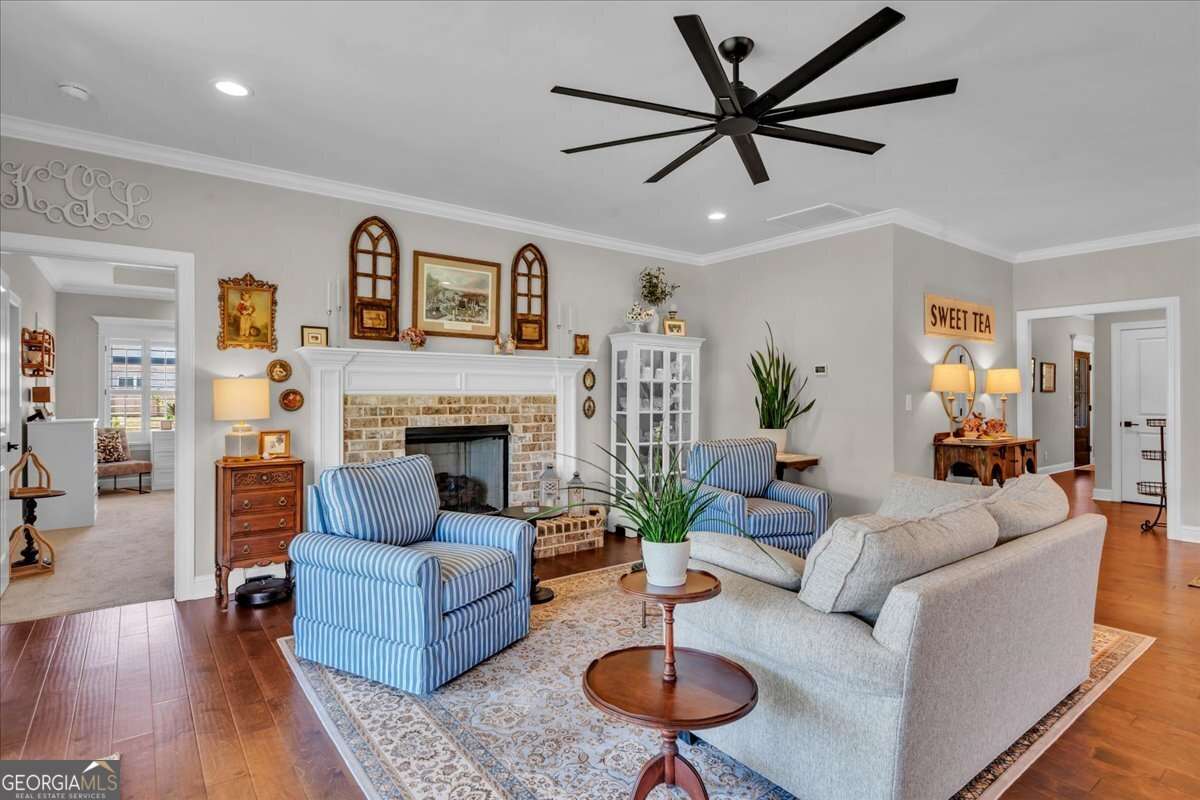 Living room with brick fireplace, crown molding, hardwood floors, and a modern ceiling fan, featuring comfortable seating and an open, inviting layout.
