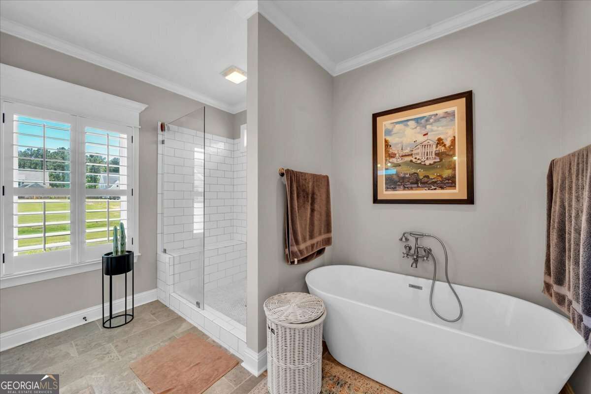 Primary bathroom featuring a freestanding soaking tub, glass-enclosed tiled shower, double windows with plantation shutters, and a clean, modern design.