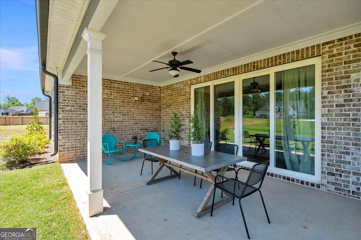 Covered back porch with brick exterior, ceiling fan, and double sliding glass doors, featuring a spacious seating and dining area overlooking a flat backyard.