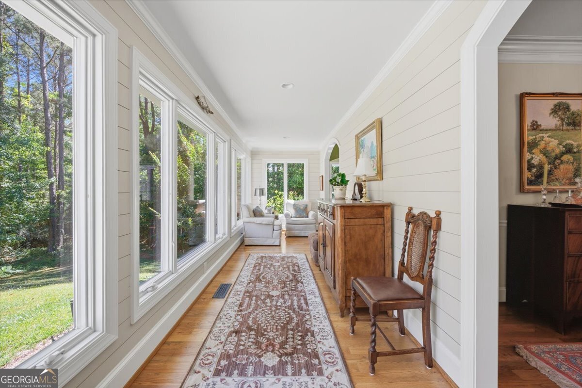 Bright sunroom hallway with hardwood floors, large picture windows, shiplap walls, and peaceful wooded backyard views at 115 Covington Place in North Macon.