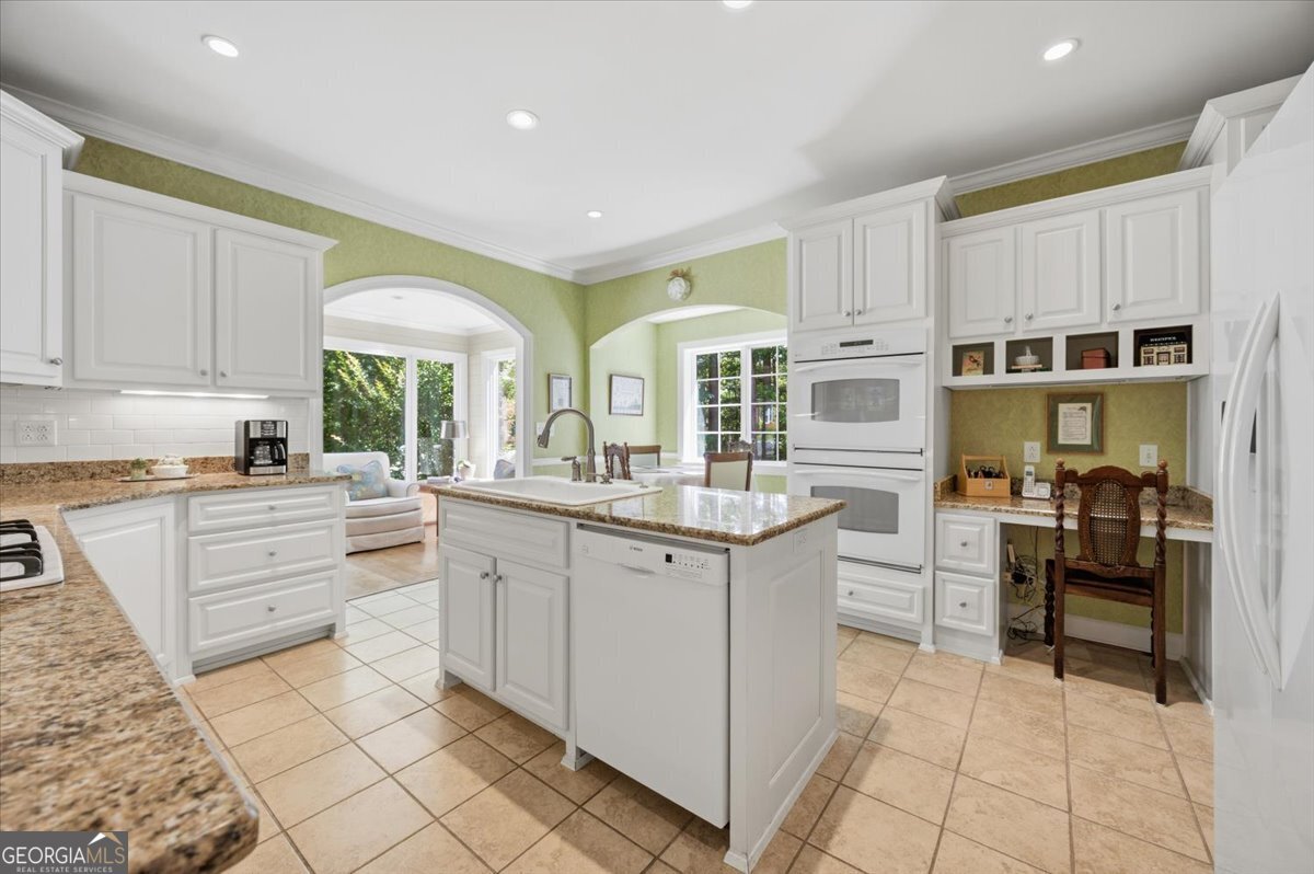 Updated kitchen at 115 Covington Place featuring white custom cabinetry, granite countertops, center island, double ovens, and built-in workspace with views into the sunroom.