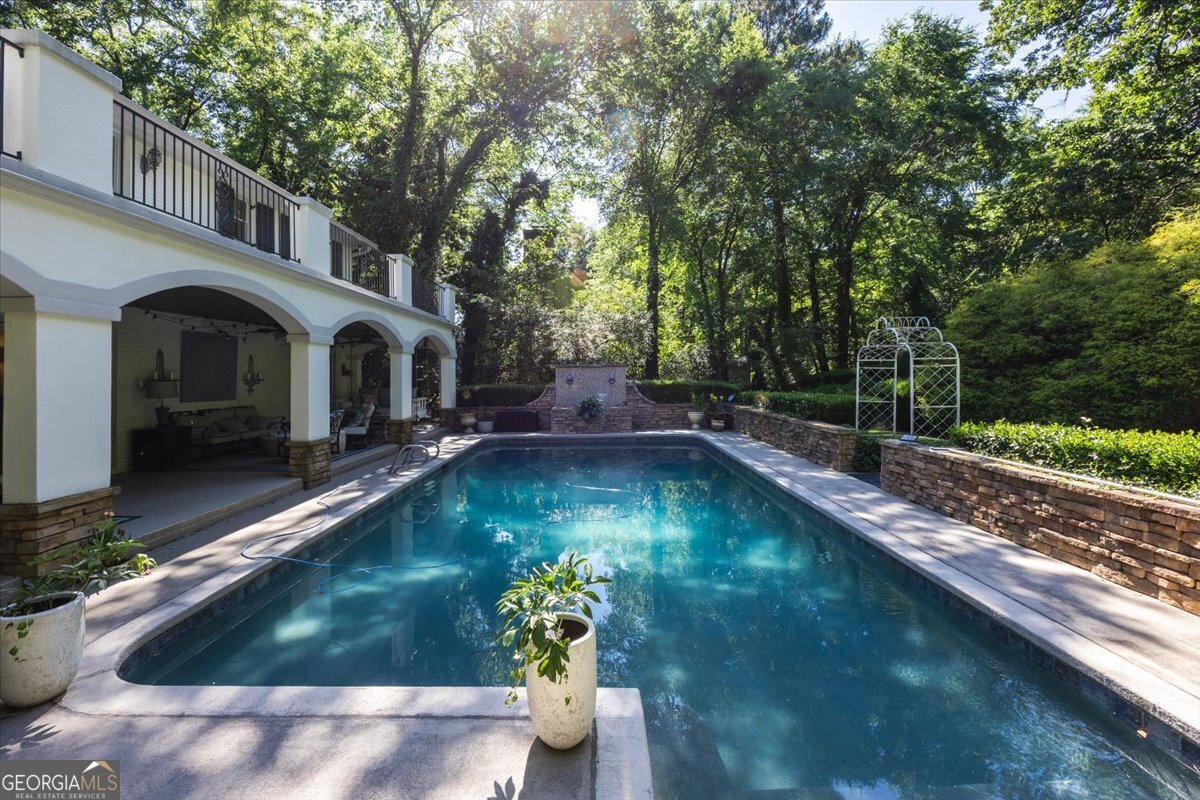Resort-style pool at 4717 Brae Burn Lane in Macon GA surrounded by mature trees, stone privacy walls, and covered outdoor living space beneath an elegant terrace balcony.