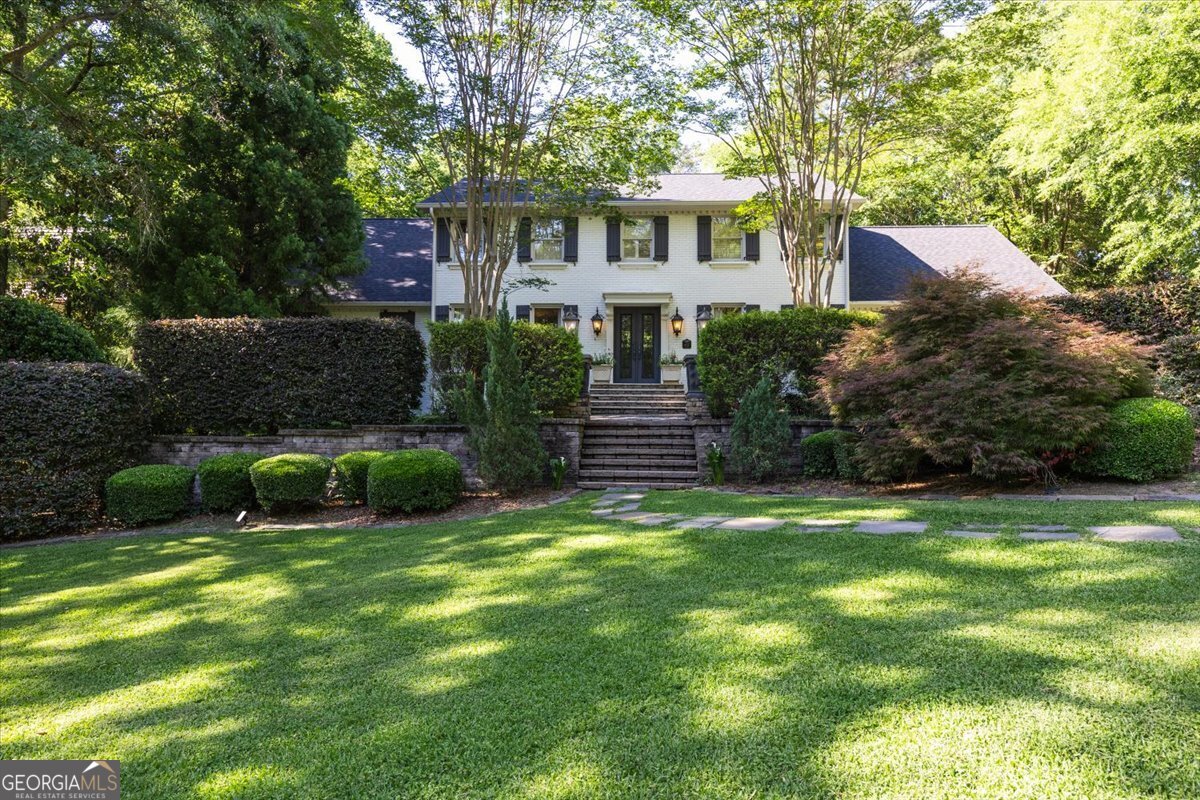 Wide exterior view of 4717 Brae Burn Lane in Saint Andrews showcasing the stately white brick luxury home, expansive manicured lawn, mature landscaping, and elegant approach in North Macon.