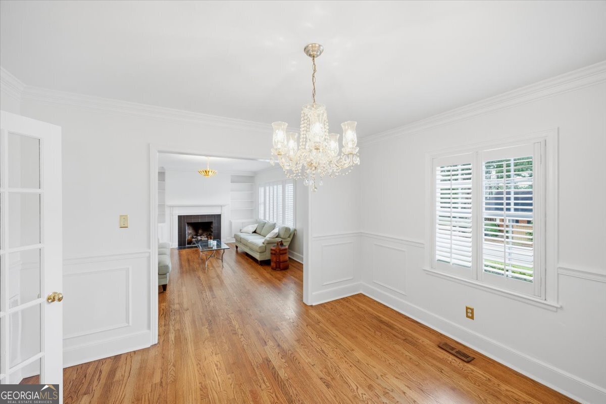 Bright formal dining room at 3561 Overlook Avenue in Midtown Macon featuring hardwood floors, elegant chandelier lighting, detailed trim work, and open flow into the living area with fireplace.