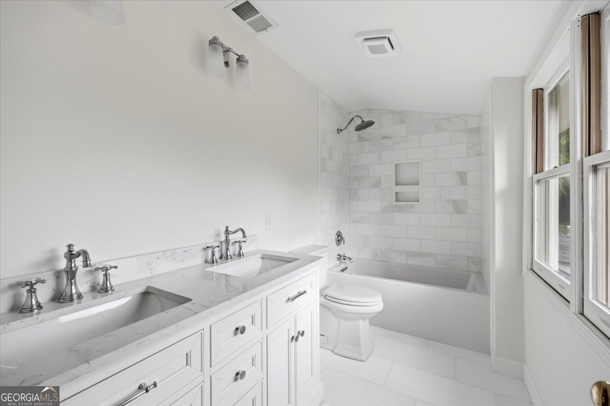 Elegant renovated bathroom at 3561 Overlook Avenue in Midtown Macon featuring double vanity, marble finishes, custom cabinetry, and beautifully tiled tub and shower surround.