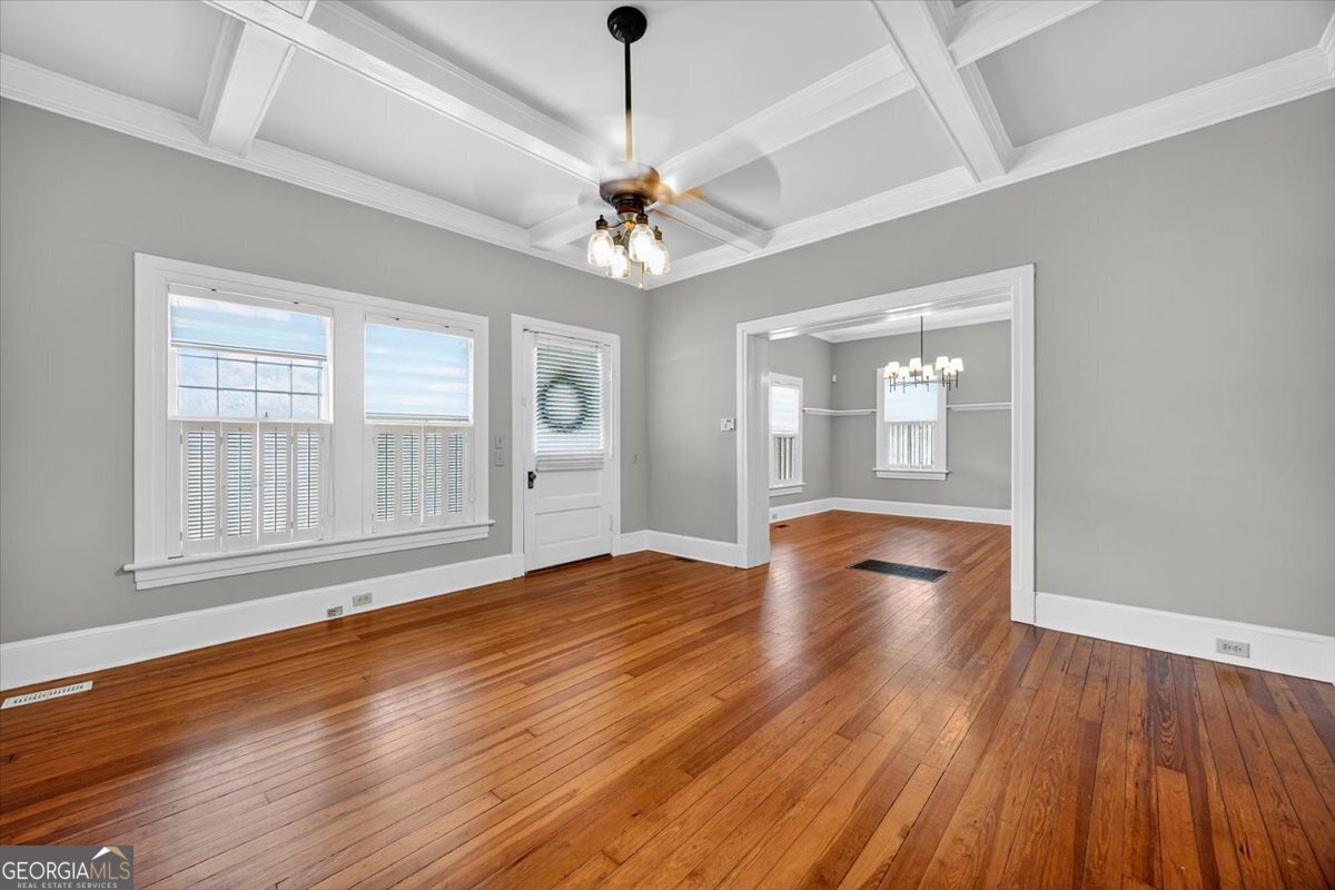 Living room at 173 Pierce Avenue in Macon, GA featuring original hardwood floors, coffered ceiling, large windows, and an open layout connecting to the dining room.