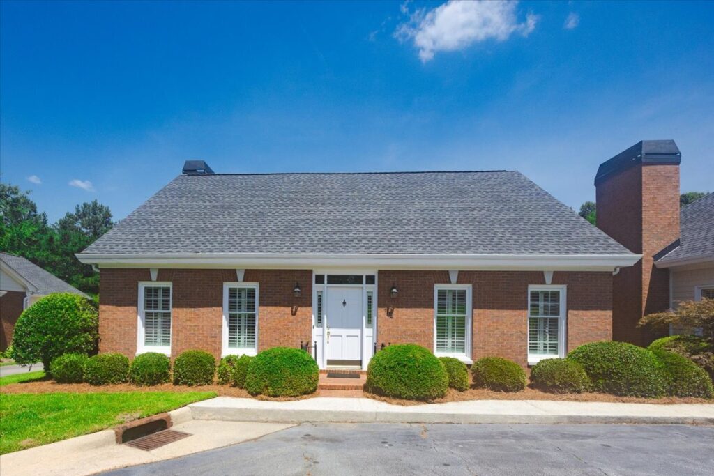 Front elevation of 104 Covington Place, a one-level brick townhome for sale in Covington Square, North Macon, featuring mature landscaping, plantation shutters, and low-maintenance exterior living.
