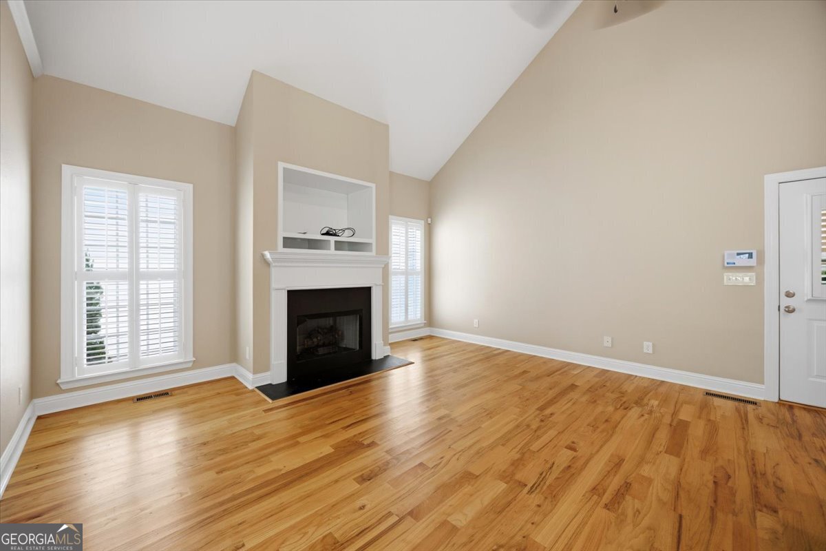 Spacious living room with soaring vaulted ceilings, hardwood floors, gas fireplace, and large windows providing abundant natural light in Madison Subdivision home in Macon, GA.
