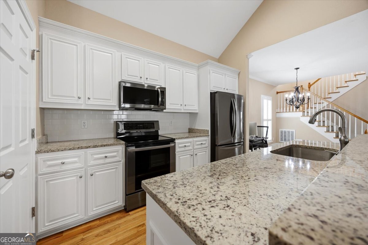 Bright open-concept kitchen with white cabinetry, granite countertops, stainless steel appliances, hardwood floors, and breakfast bar in Madison Subdivision home in Macon, GA.