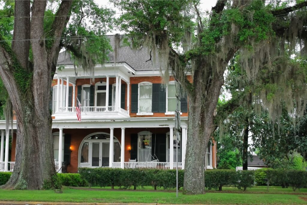 Historic Georgia home with wraparound porch, brick exterior, and mature oak trees draped in Spanish moss