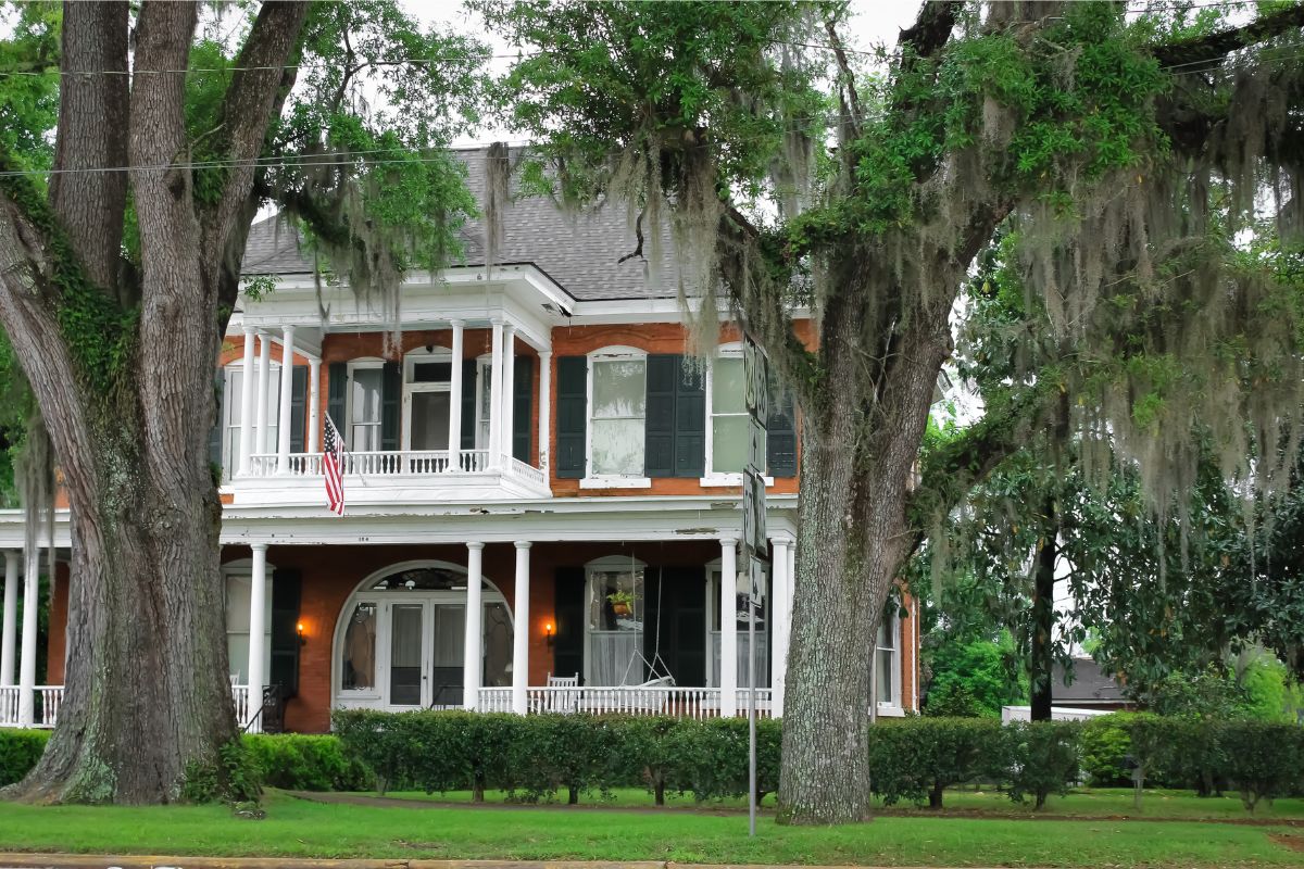 Historic Georgia home with wraparound porch, brick exterior, and mature oak trees draped in Spanish moss
