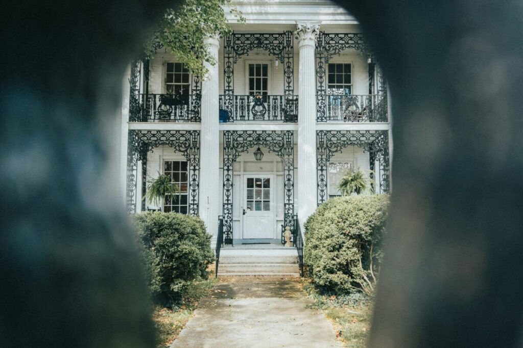 Here's What Happens When You Hire JoJo - Joanna "JoJo" Jones Elegant home viewed through an open gate representing the home buying and selling journey with JoJo Jones