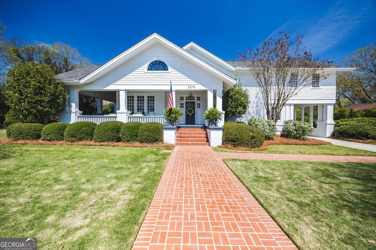 : Beautiful white Ingleside Midtown home with a welcoming covered front porch, brick walkway, manicured landscaping, and classic Southern architecture in Macon, Georgia.