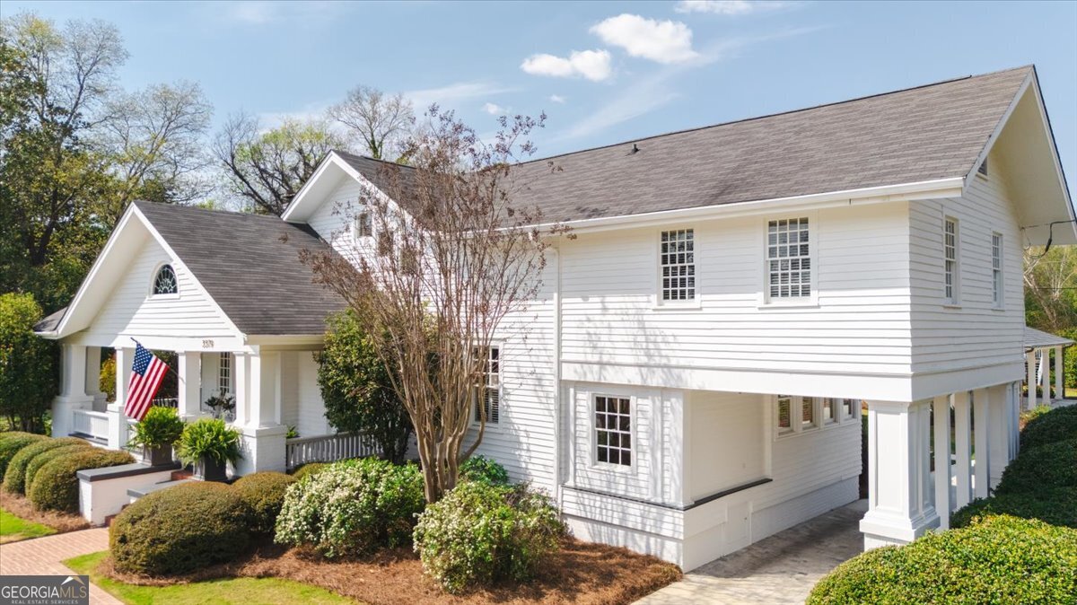 Angled exterior view of a beautifully renovated Ingleside Midtown home featuring classic white architecture, covered front porch, landscaped grounds, and a spacious three-car portico in Macon, Georgia.