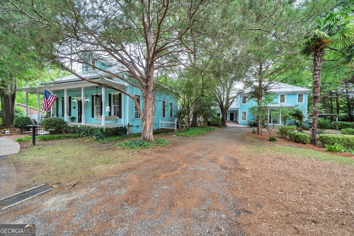 Beautiful renovated Southern home with a rocking chair front porch, mature shade trees, covered breezeway, and spacious detached guest house in a private landscaped setting.
