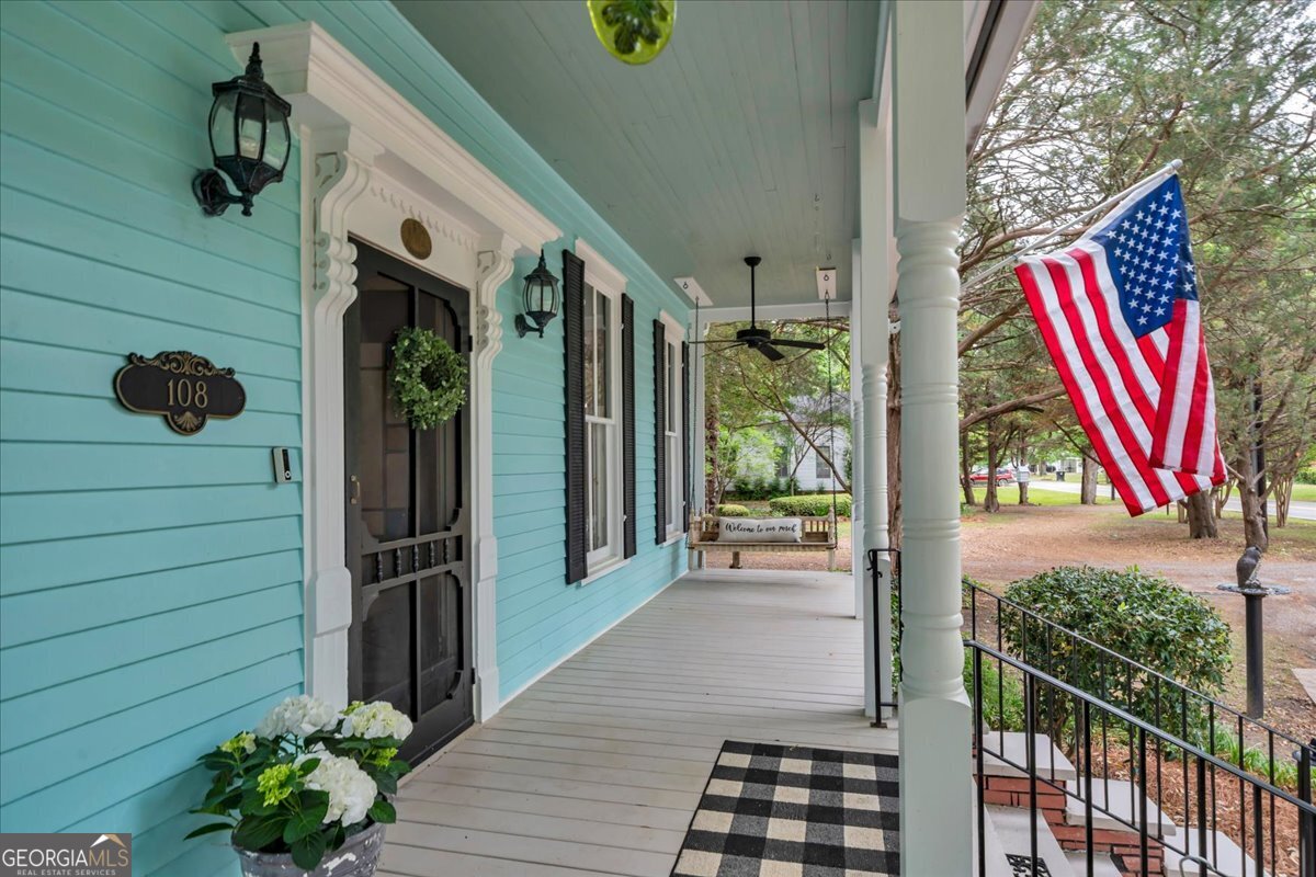 Inviting Southern rocking chair front porch with decorative trim, screened front door, porch swing, classic columns, and American flag.