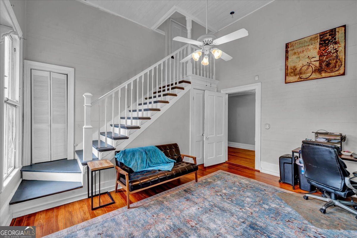 Bright living room with soaring ceilings, original hardwood floors, elegant staircase, and historic architectural details filled with natural light.