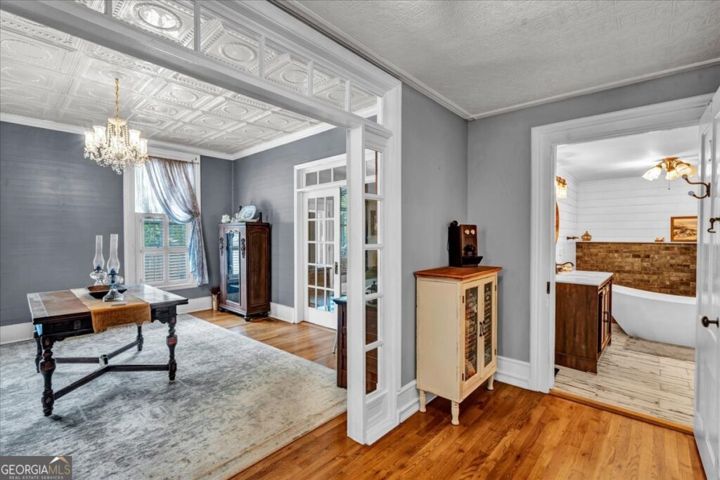 Elegant formal dining room with ornate tin ceilings, crystal chandelier, hardwood floors, French doors, and a beautifully renovated spa-inspired bathroom nearby.