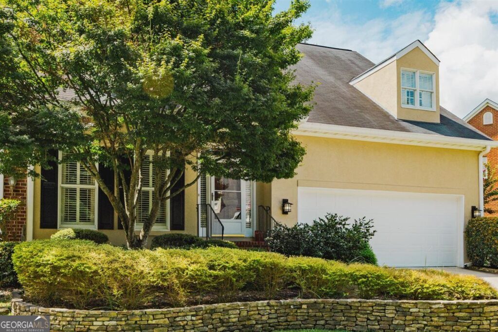 Front Exterior of 155 N. Wellington | Wellington Home for Sale in North Macon - Joanna "JoJo" Jones Front exterior of 155 N. Wellington in the Wellington Subdivision, featuring a stucco façade, two-car garage, mature trees, and professionally landscaped front yard in North Macon.