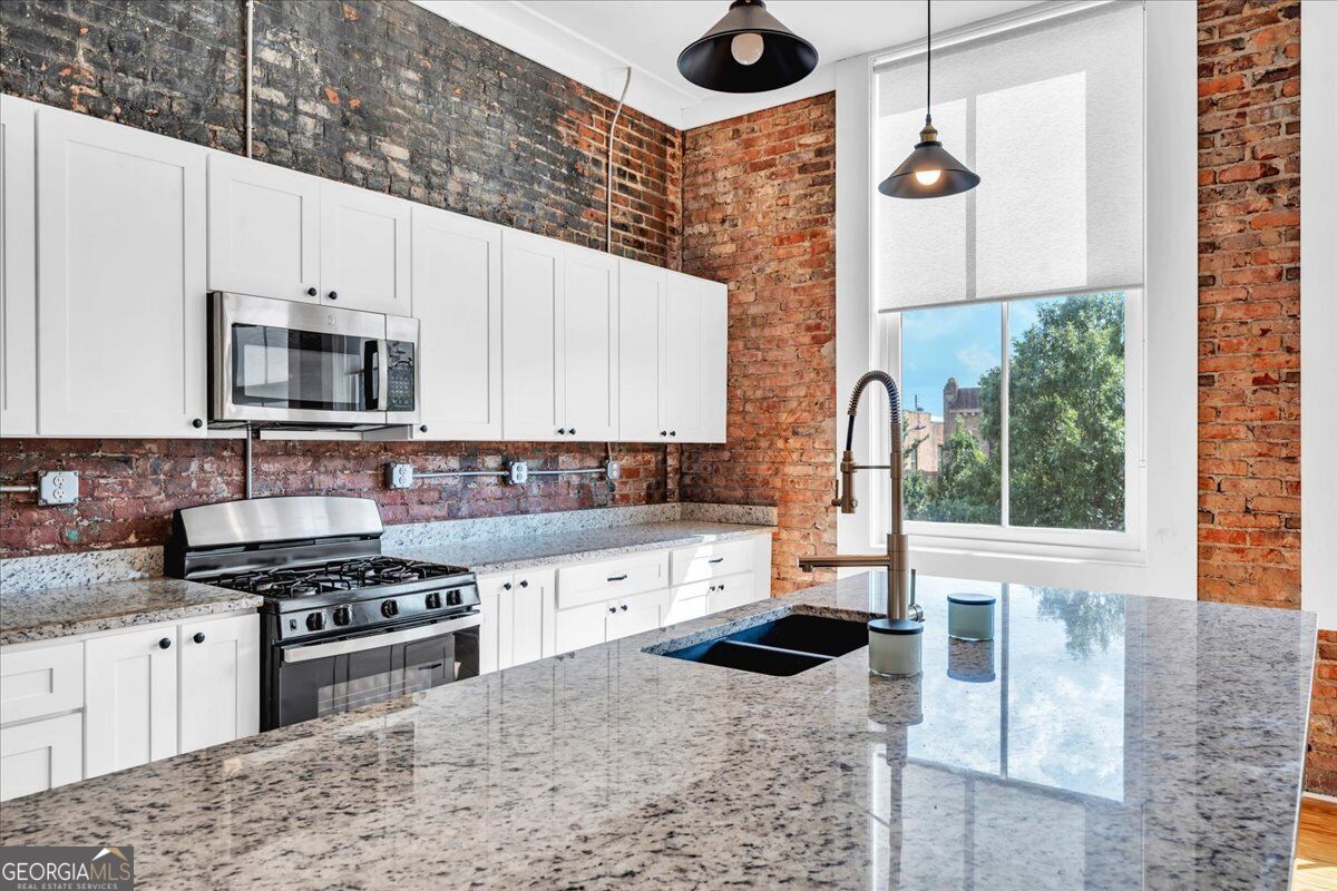 Renovated kitchen at 565 Poplar Street in Macon, GA, featuring exposed historic brick, white cabinetry, granite countertops, stainless steel appliances, and a large island.