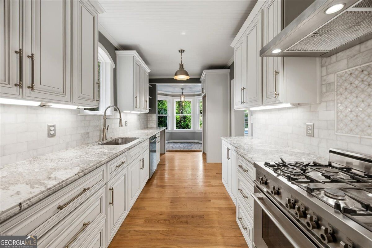 Renovated kitchen at 3860 Ridge Avenue in Macon, GA, featuring white cabinetry, stone countertops, hardwood floors, stainless steel appliances, and a professional-style gas range.