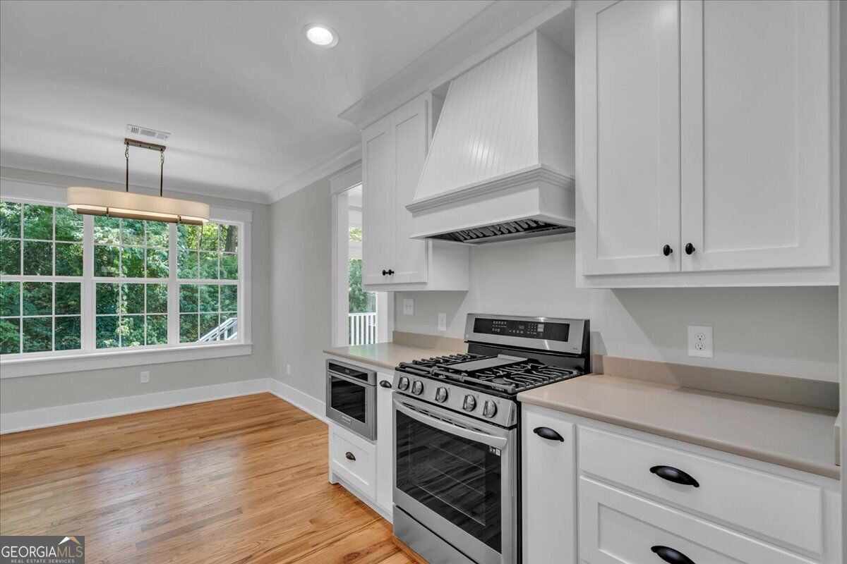 Kitchen at 203 Oberon Place N in Macon, GA, featuring white cabinetry, solid surface countertops, stainless steel appliances, hardwood floors, and a bright breakfast area.