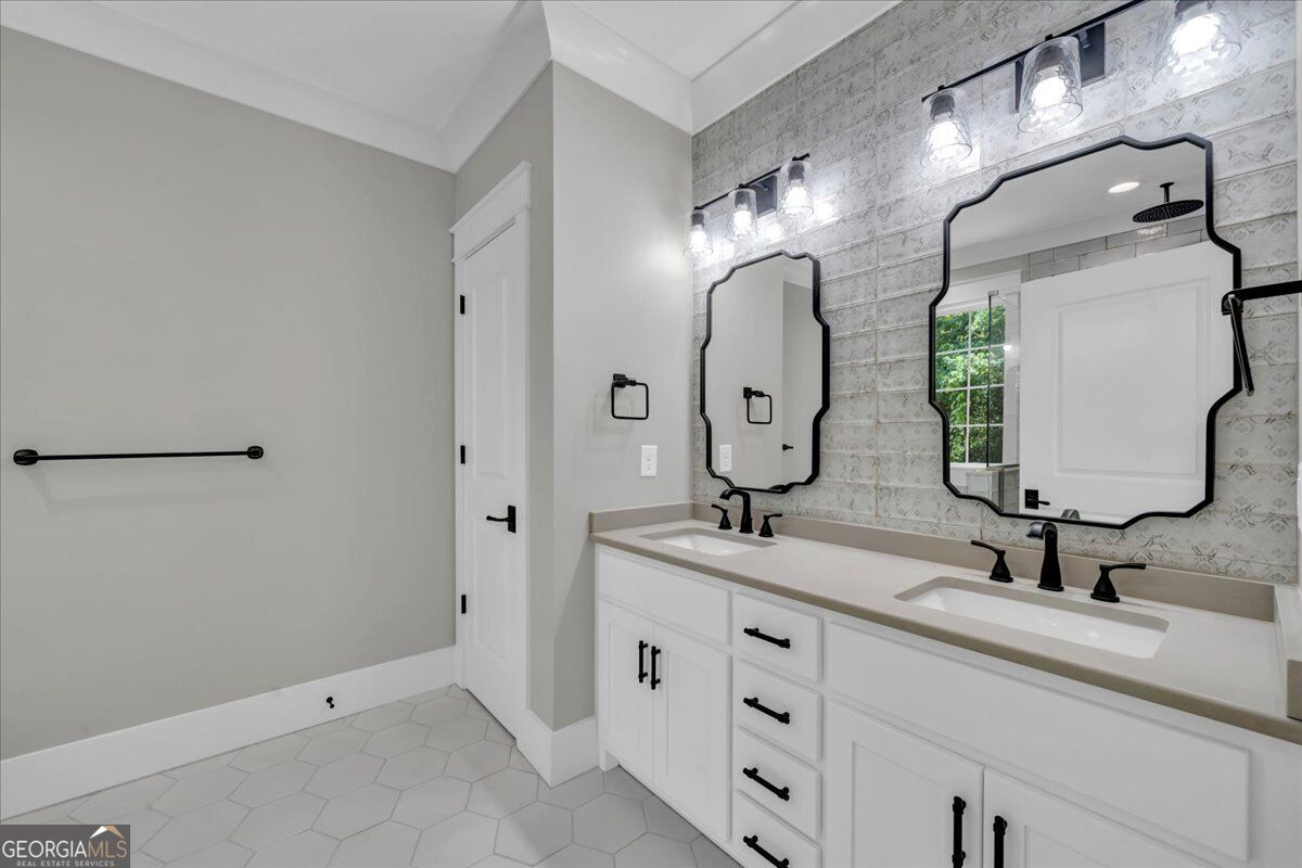 Double vanity bathroom at 203 Oberon Place N in Macon, GA, featuring white cabinetry, dual sinks, decorative mirrors, black fixtures, and patterned tile.