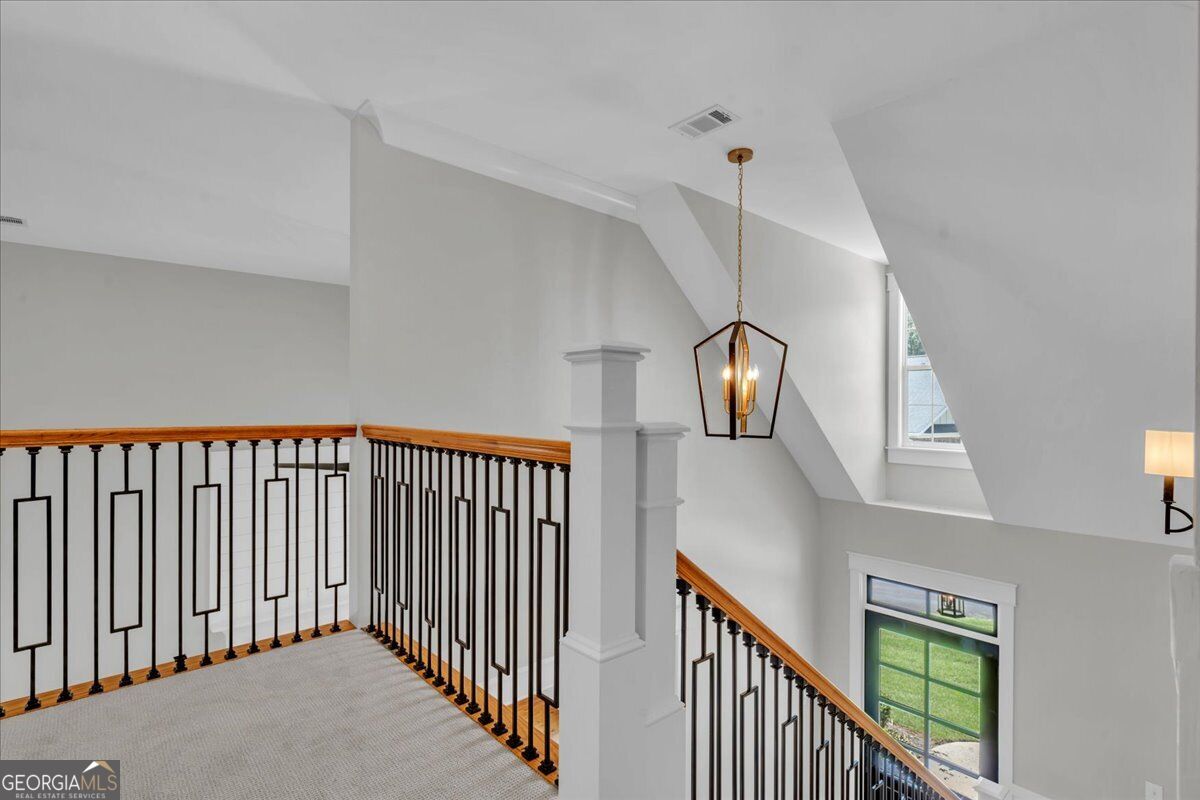 Upstairs landing and staircase at 203 Oberon Place N in Macon, GA, featuring decorative iron railings, wood handrails, and a statement pendant light.
