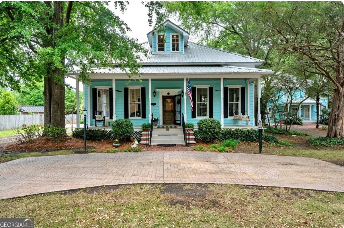 Beautifully renovated historic Southern home with a wraparound rocking chair porch, metal roof, mature shade trees, and private landscaped grounds.