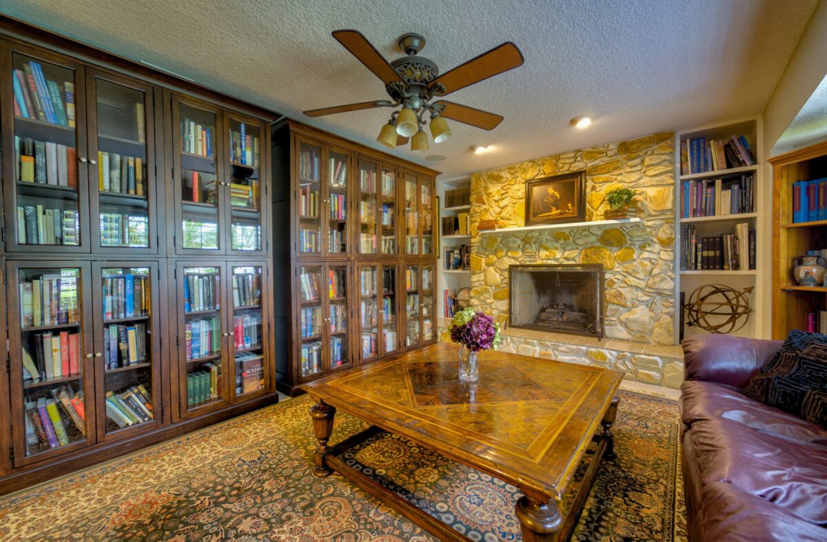 Traditional home library with built-in bookshelves, stone fireplace, and reading area