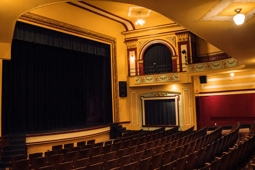 Interior of the historic Douglass Theatre in Macon, Georgia, featuring the stage, ornate balcony, warm golden architectural details, and rows of wooden auditorium seats.