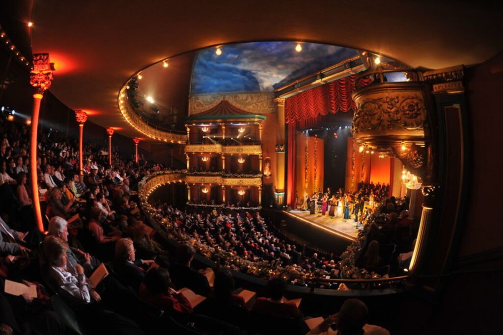 Audience watching a live performance inside the historic Grand Opera House in Macon, Georgia, surrounded by ornate balconies and architectural details.