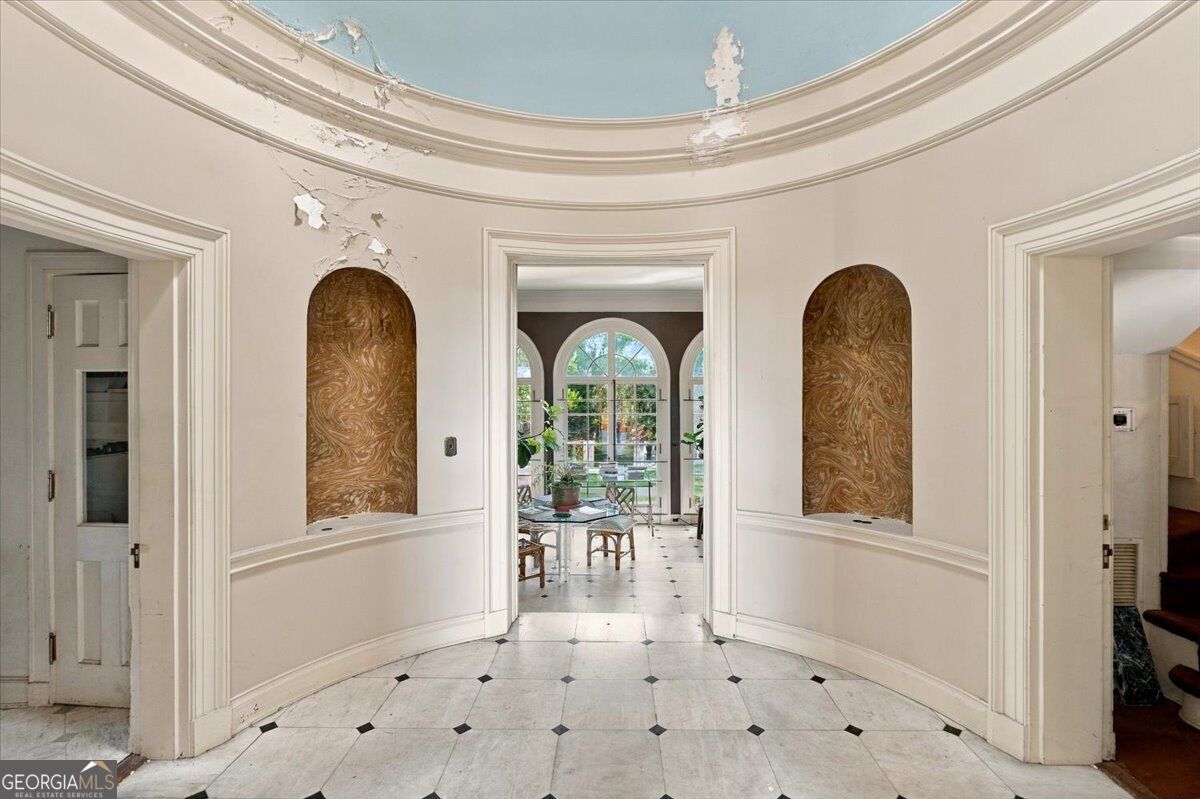 Curved entrance hall at Villa Albicini in Macon GA, featuring decorative wall niches, patterned tile flooring and a view into the garden room.