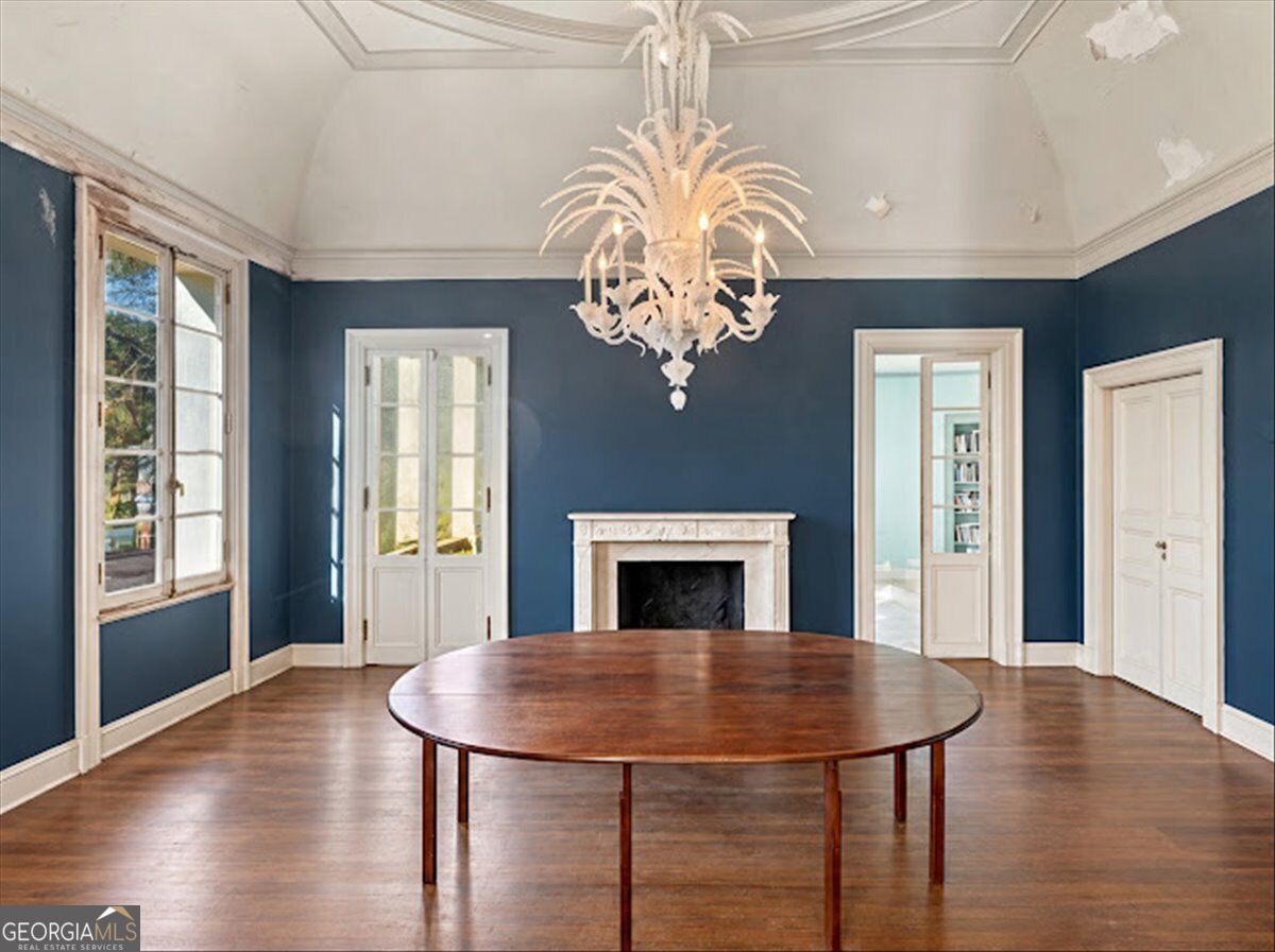 Formal dining room at Villa Albicini in Macon GA, featuring blue walls, an ornate chandelier, a white fireplace mantel and hardwood floors.