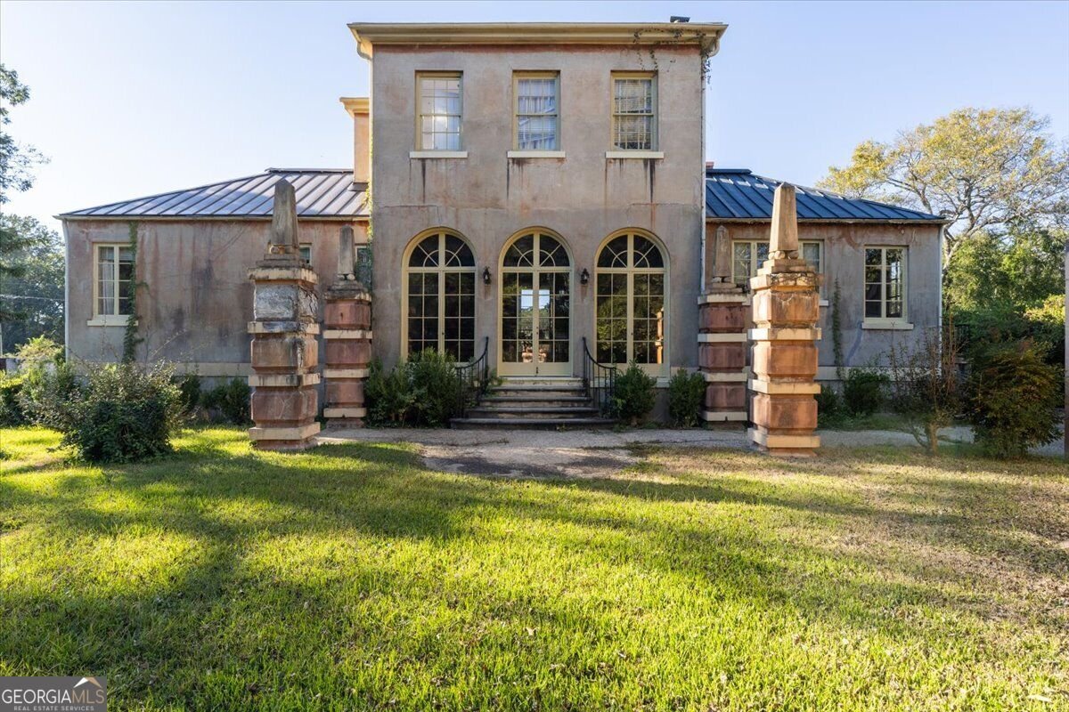 Garden side of Villa Albicini in Macon GA, featuring arched French doors, entrance steps, decorative masonry pillars and a lawn.