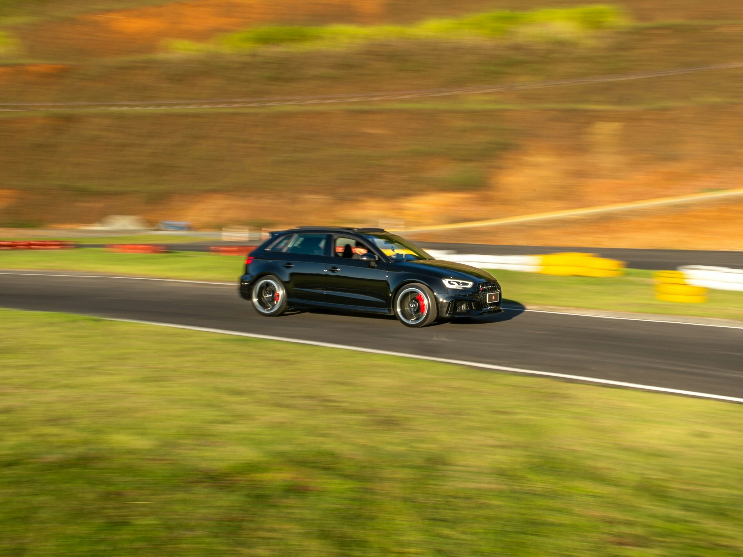 Audi vehicle — illustrative image accompanying Middle Georgia manufacturing news Black Audi driving on a racetrack against a motion-blurred backdrop of golden autumn foliage.